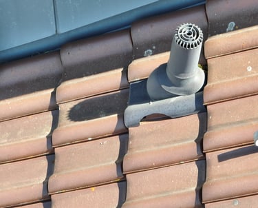 A grey ventilation pipe installed on a brown ceramic tile roof for attic exhaust.