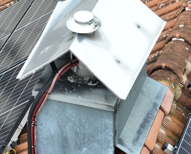 drone picture of a stainless steel chimney cap and vent installed on a tiled roof near solar panels.
