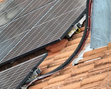 Close-up of residential solar panels installed on a clay tile roof with visible electrical wiring and mounting brackets.