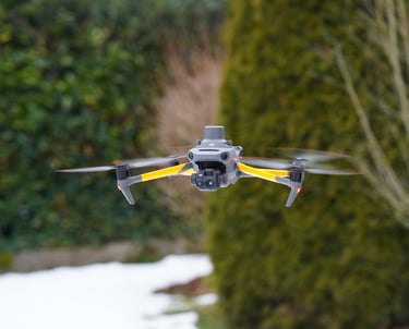 Professional DJI Mavic 3 thermal drone hovering outdoors against a blurred green hedge background.