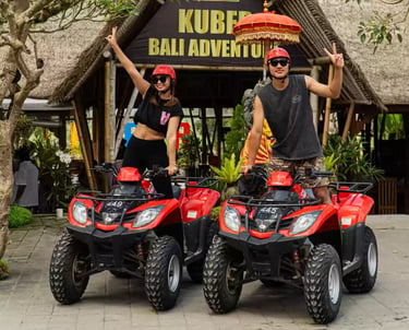 A couple poses on red ATVs for a Kuber Bali Adventure tour in a tropical jungle setting.