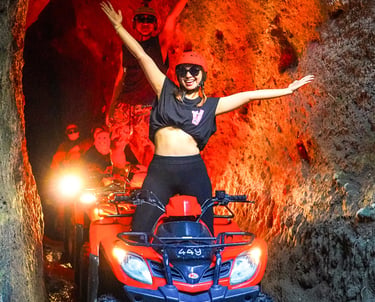 Excited tourists riding red ATV quad bikes through a narrow rock tunnel cave in Bali.