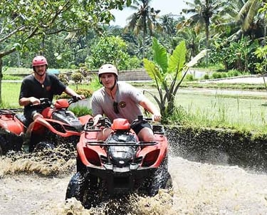 Two men riding red ATVs through a muddy river on a jungle quad bike tour in Bali.