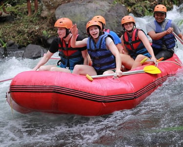 A group of cheerful tourists wearing life jackets and helmets on a white water rafting adventure in a red boat.