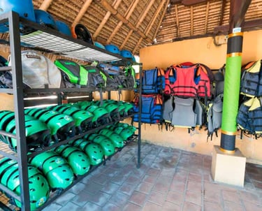 Rows of green safety helmets and life jackets for river rafting stored in an outdoor gear hut.