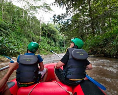 Two people wearing helmets and life jackets white water rafting down a river in a lush Bali jungle.