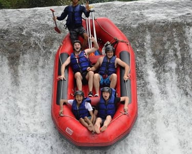 Excited group of tourists on a white water rafting adventure descending a waterfall in a red inflatable boat.