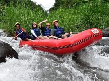 Excited group white water rafting in a red boat through river rapids with lush greenery.