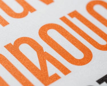 Abstract close-up of high-quality printed materials with bold typography and orange ink, focusing on texture and professional finish.