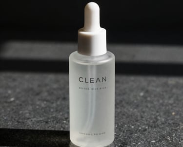 Clean, minimalist bottle design for a high-end skincare line, photographed with soft natural light and deep shadows on a dark stone surface.