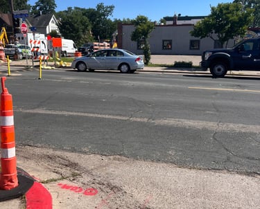 Silver sedan on George Floyd Square construction zone with orange cones and utility trucks.