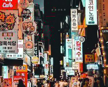 Vibrant night scene of a crowded Seoul street filled with glowing neon Korean business signs and pedestrians.