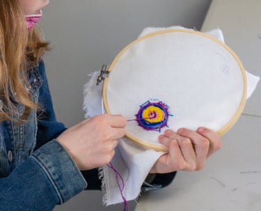 Young girl pulling thread through fabric to create an embroidered spider web.