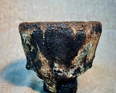 A handbuilt chawan cup for tea ceremony with black, brown and green stone matt texture