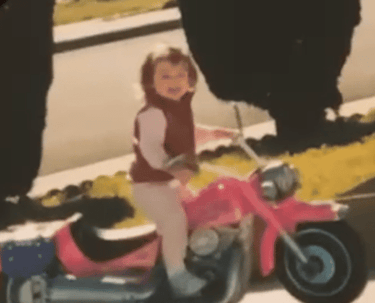 a little girl riding a pink motorcycle in a driveway