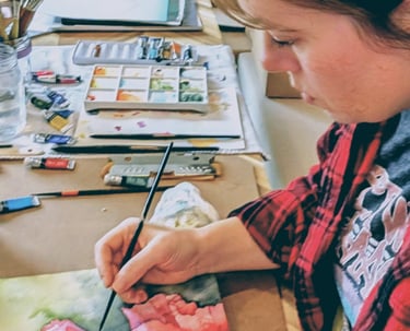 Artist painting a vibrant pink watercolor floral painting  in a home art studio setup.