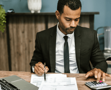 Homme en costume assis à son bureau, tenant un stylo et utilisant une calculatrice