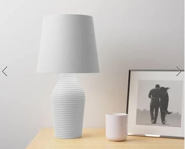 Modern white ribbed ceramic table lamp with fabric shade on a wooden nightstand.