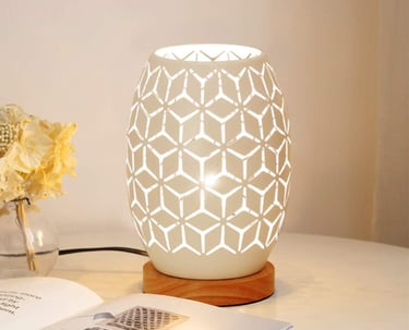 Modern white ceramic table lamp with geometric cutouts and a wooden base on a bedside table.