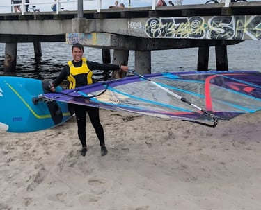 Lennard holding a colorful windsurf board on the beach before heading into the water