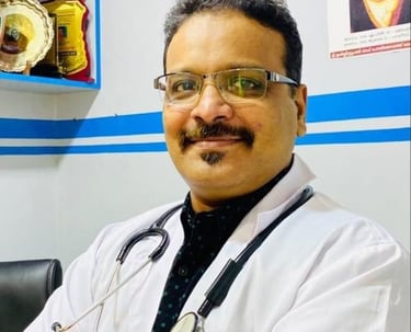 A smiling male doctor wearing a white lab coat and stethoscope in a medical clinic office setting.
