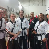 Martial arts students in traditional uniforms posing with training weapons in a studio.