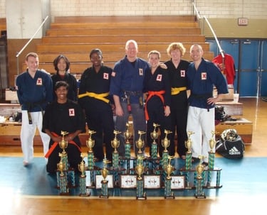 Martial arts team in traditional uniforms posing with trophies after a karate tournament competition.