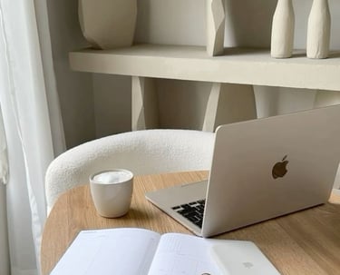 Minimalist home office setup with a laptop, open notebook, coffee cup, and shelves in the background