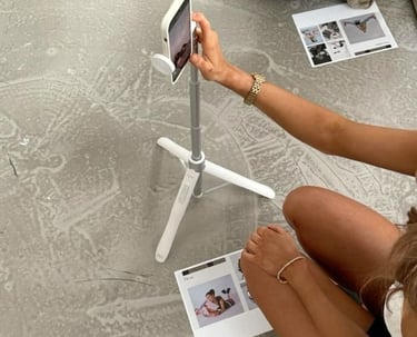 Woman filming content with a phone on a tripod and printed materials on the floor.