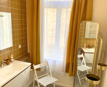 Salle de bain élégante avec carrelage jaune, lavabo moderne et grande fenêtre.