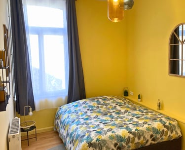 Chambre lumineuse avec lit double et mur jaune dans maison meublée.
