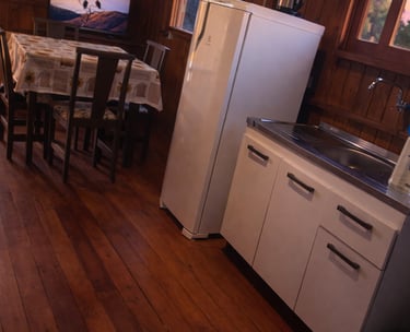 parte interna da cabana, a cozinha, com geladeira, pia, armários, mesa e TV 