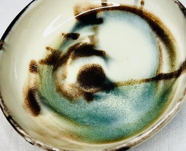 A glazed plate with black lid and abstract brown and green spots and shades