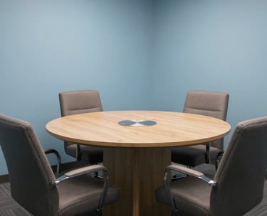 A private, professional consultation room in a North American / US office. A round table sits in the center with comfortable chairs. The walls are a calming Light Blue, suggesting a trustworthy and safe space for legal discussions.