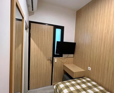 Kamar premium Kos Si Bos dengan meja kerja, kursi, lemari besar, dan Smart TV terpasang di dinding.