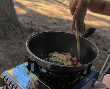 Stirring onions in a frying pan over a camping stove on a forested campsite