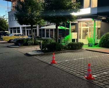 Illuminated entrance of Hotel Thannhof in Germany with a paved parking lot and classic cars.