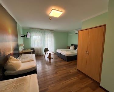 Spacious hotel room with twin beds, wooden wardrobe, desk area, and a large sunset wall mural.