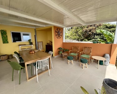 Modern outdoor patio with a wooden dining table, colorful chairs, and tropical decor overlooking lush greenery.