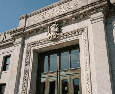 A close-up photograph of the architectural details of the Robert F. Kennedy Department of Justice Building in Washington D.C., focusing on the heavy bronze doors and classic limestone carvings, clear blue sky background, North American / US.