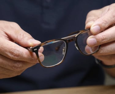 A close-up of a pair of handcrafted glasses being polished by an artisan, highlighting the detail and quality expected of the profession. Neutral palette with dark navy backgrounds. North American / US / Indiana.