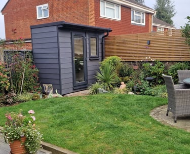 Modern grey garden office pod situated in a landscaped backyard with lawn and patio furniture.
