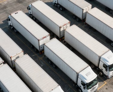 An aerial view of a clean, organized logistics yard in North America with white semi-trailers precisely lined up. Morning sunlight casting soft shadows on the pavement.