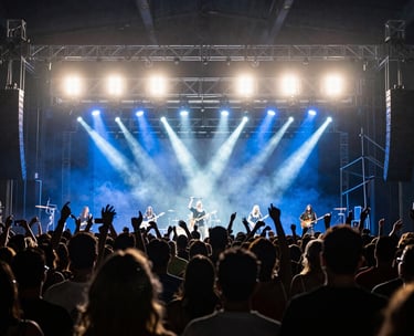 Action shot of a live concert production in Brazil, showing the silhouette of the crowd against bright steel blue and white stage lights, professional photography style.