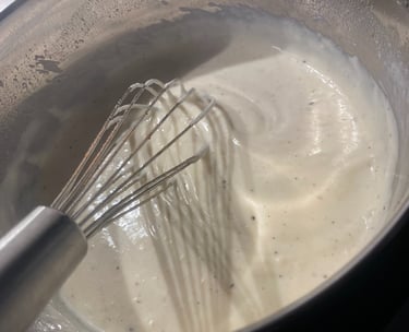 Pouring fresh milk into a pan with roux and a metal whisk to make homemade white sauce.