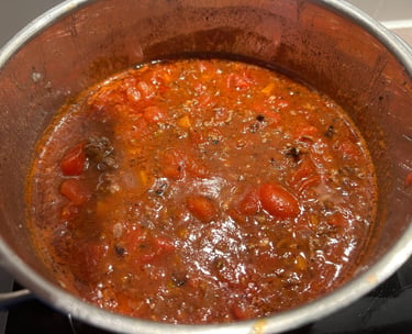 Homemade bolognese meat sauce with chunks of tomato simmering in a stainless steel pot on a stove.