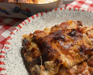 A portion of homemade beef lasagna with melted cheese on a plate over a red checkered tablecloth.