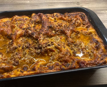 Freshly baked homemade beef lasagna with melted cheese and rich tomato sauce in a black baking dish.