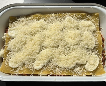 Homemade lasagna layers topped with fresh mozzarella slices and shredded parmesan cheese in a white baking dish.