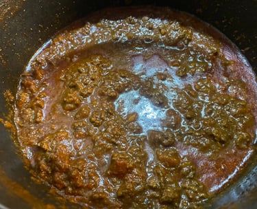 Rich and chunky homemade bolognese sauce simmering in a black pot, featuring ground beef and tomato base.